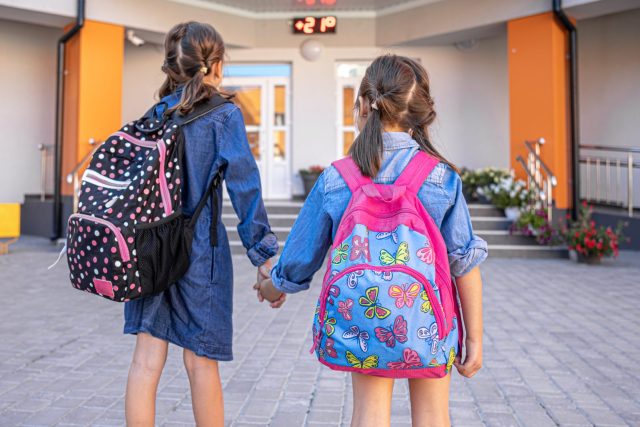 Dos niñas con mochila entrando de la mano en el colegio